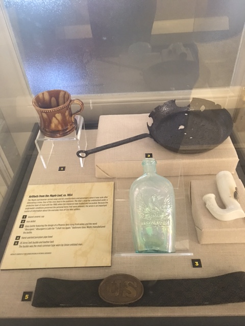 A collection of items from The Maple Leaf including a frying pan, belt, ceramic pipe, and other everyday items used by sailors.